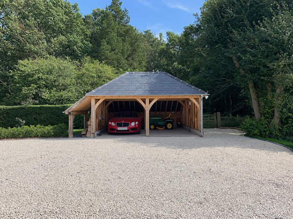 Oak framed 2 bay garage with hipped roof and logstore to left hand side, by Shires Oak Buildings