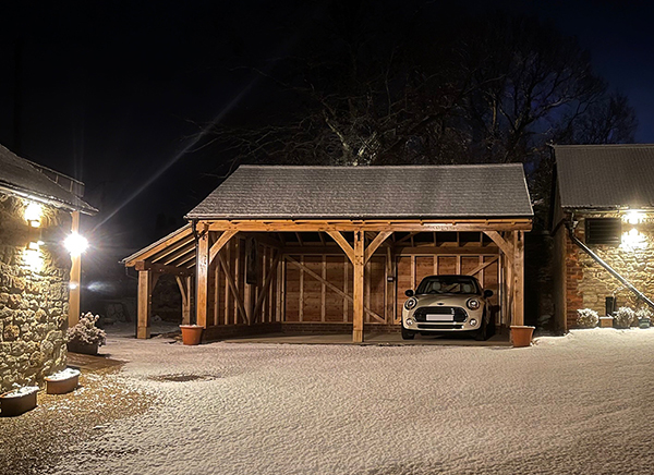 Oak framed 2 bay garage with logstore, at night, by Shires Oak Buildings